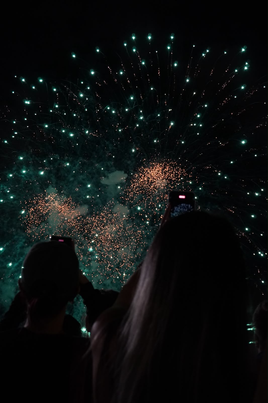 Audience filming green fireworks overhead